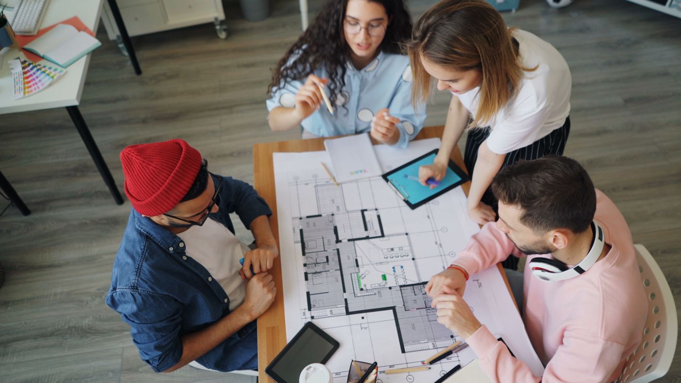 Four studio colleagues discussing floor plans, materials and a tablet around a table